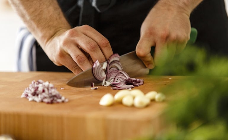 Man slicing onion and garlic, both of which are foods that cause body odor