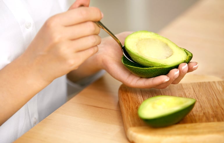 Woman scooping avocado from skin to make a vegan easy gazpacho recipe