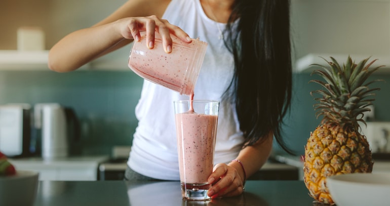 Woman pouring fruit smoothie into a glass for protein, carbs, and healthy fats