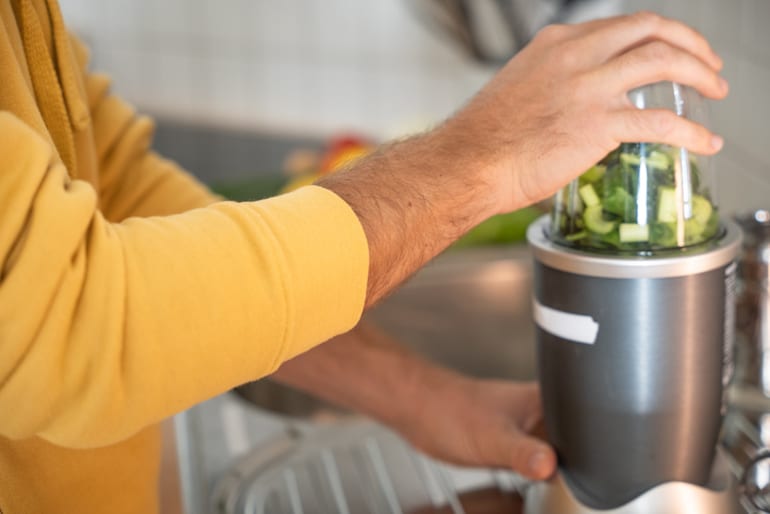 Man making a smoothie with fruits and green vegetables