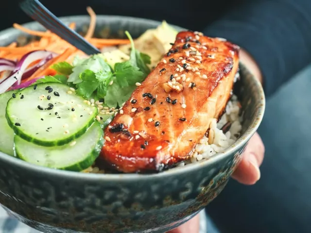 Person eating a salmon, one of the healthiest fish to eat, in a poke bowl