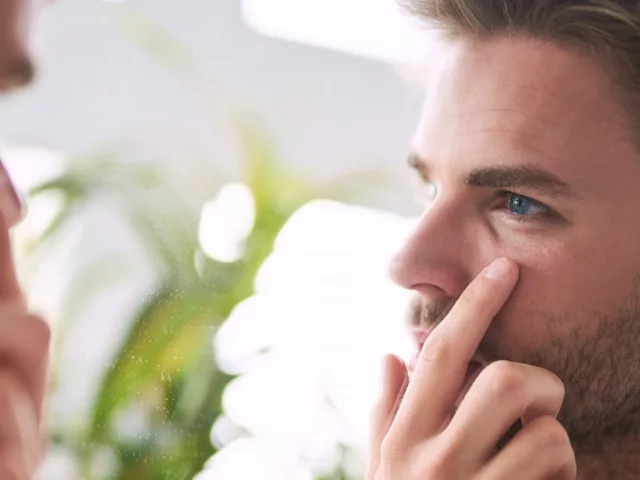 Man investigating wrinkles in mirror, wondering about the best time to take collagen