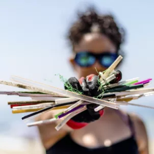 Woman holding up plastic straws on a Surfrider Foundation beach cleanup to protect ocean