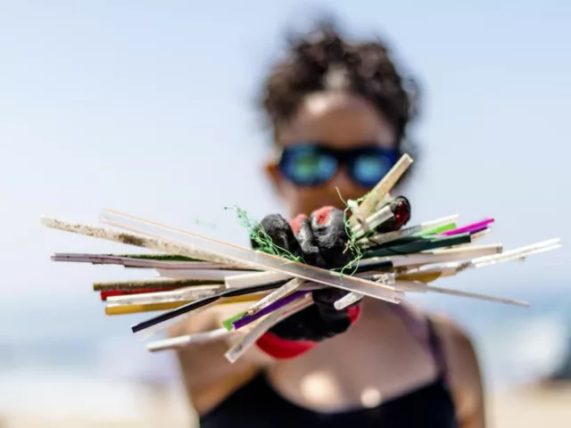 Woman holding up plastic straws on a Surfrider Foundation beach cleanup to protect ocean