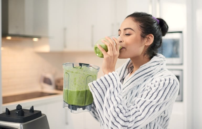 Woman drinking smoothie with greens, which is healthier than juicing