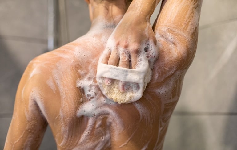 Woman washing her back in the shower with the best body acne treatments