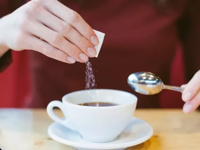 woman putting sweetener in coffee