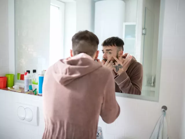 Man popping a pimple in the mirror, hoping to heal the inflammation