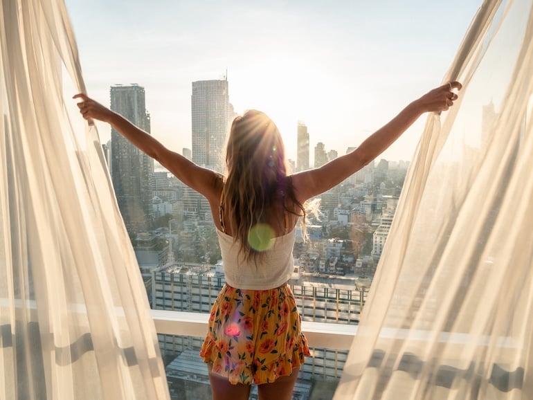 woman opening curtains in bright light