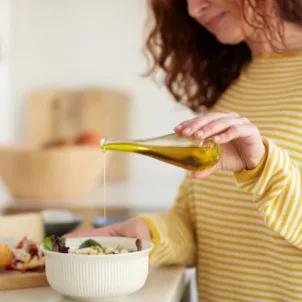 Woman drizzling olive oil onto her meal to help with PMS