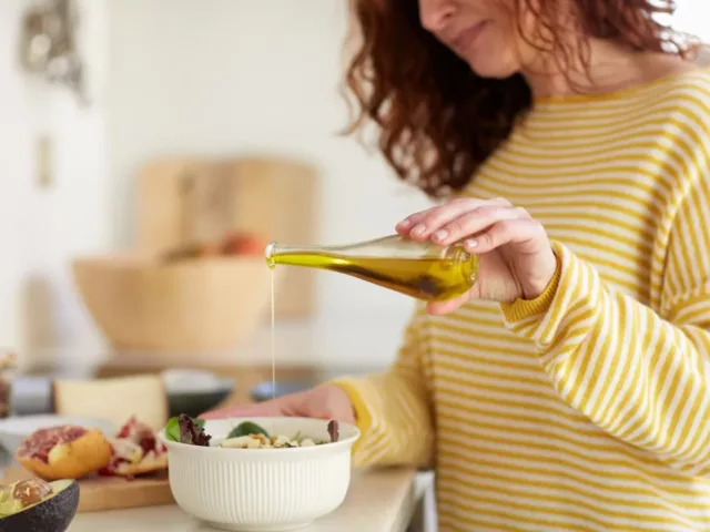 Woman drizzling olive oil onto her meal to help with PMS