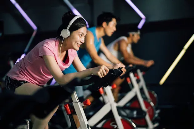 Woman at a spin class looking happy because she has PMS symptom relief from learning how to cycle sync