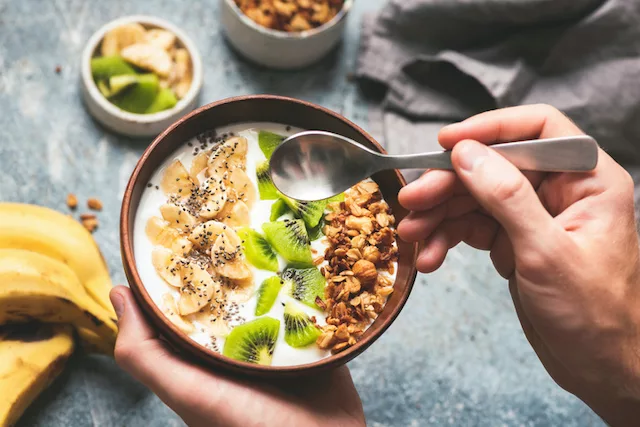Hombre comiendo yogur griego probiótico con frutas ricas en prebióticos