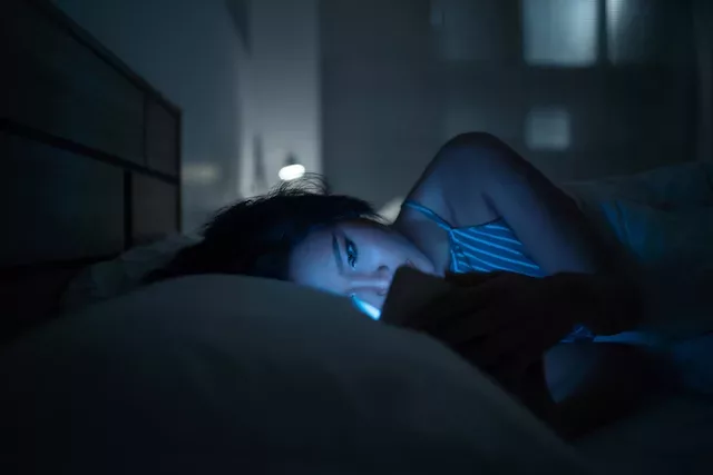 Woman on her phone struggling to sleep in bed due to blue light exposure