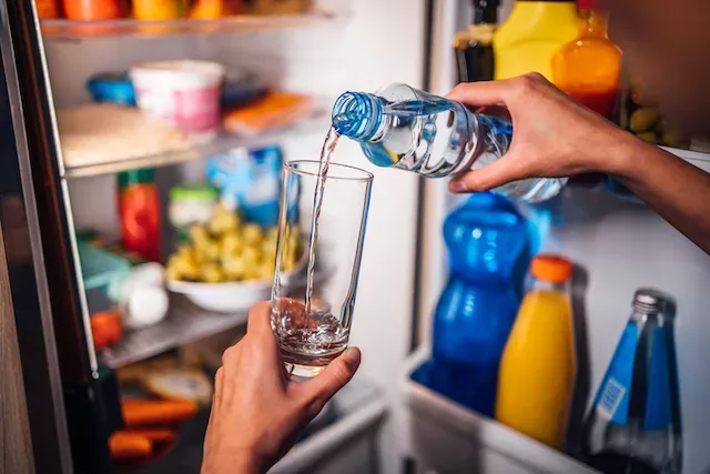 Woman pouring water into glass to support digestion while she sleeps